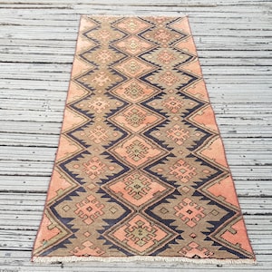 May include: A long rectangular runner rug featuring a repeating geometric diamond pattern in shades of peach, charcoal grey, and muted brown. The design includes intricate stepped edges and small central motifs within each diamond shape.
