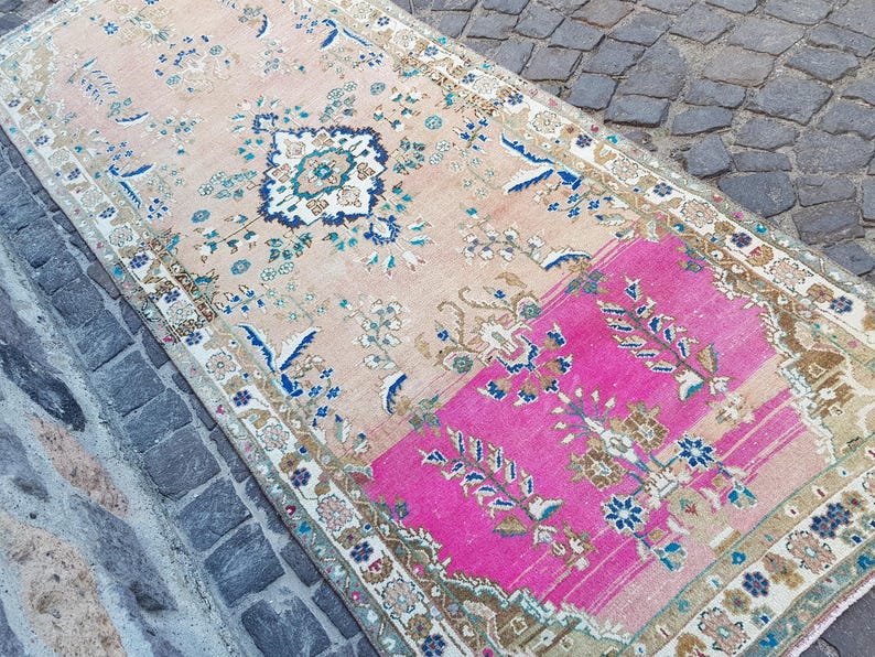 May include: A rectangular area rug featuring a faded peach background with a prominent section of vibrant hot pink. The rug is decorated with intricate floral and geometric patterns in shades of navy blue, cream, and muted brown throughout.