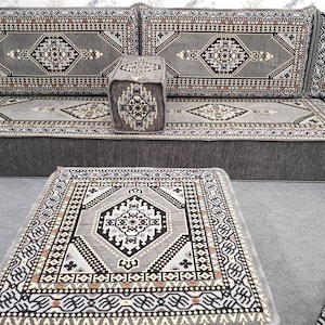 May include: A gray sectional sofa with matching ottoman and a small square pouf. The furniture features a geometric pattern in shades of gray, black, and brown. The design is reminiscent of traditional rug motifs.