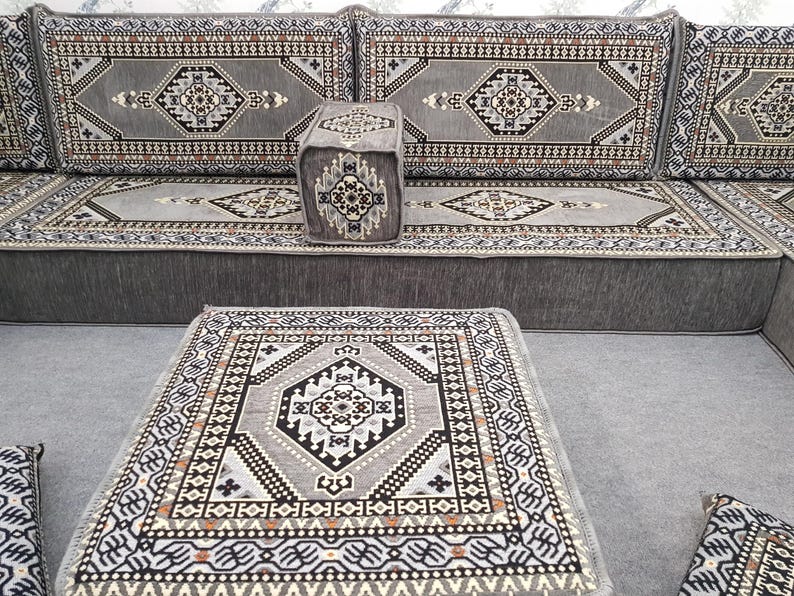 May include: A gray sectional sofa with matching ottoman and a small square pouf. The furniture features a geometric pattern in shades of gray, black, and brown. The design is reminiscent of traditional rug motifs.