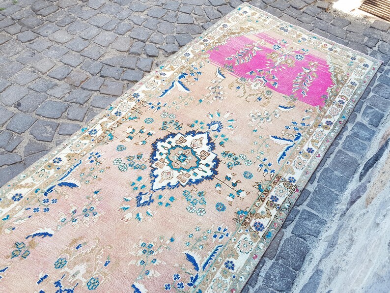 May include: A rectangular area rug featuring a light peach base with a prominent hot pink section at one end. The rug displays a central dark blue and white floral medallion surrounded by intricate botanical patterns in shades of blue, teal, and beige.