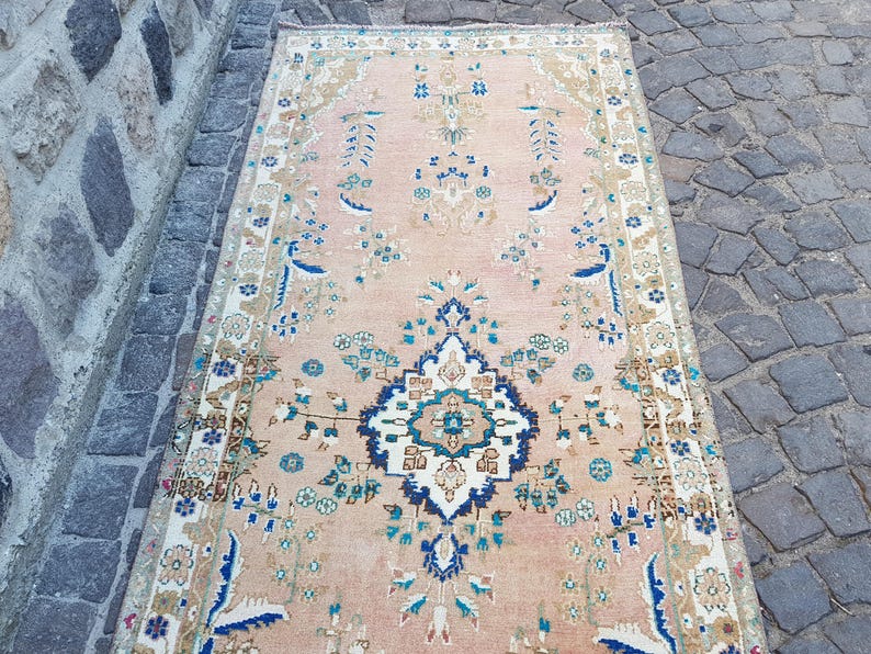 May include: A rectangular area rug featuring a soft peach background with a central dark blue and white floral medallion. The rug is decorated with symmetrical botanical patterns in shades of blue, green, and beige, framed by a detailed border.
