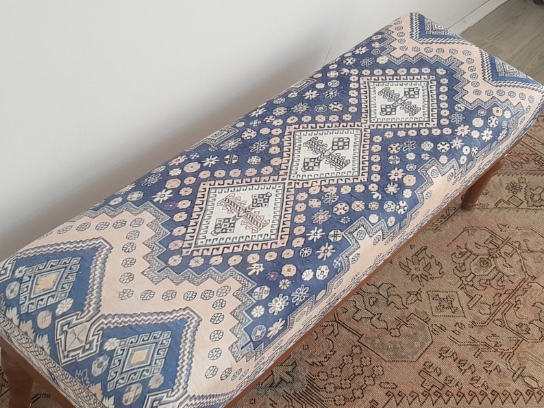 May include: A blue and pink patterned bench with a wooden frame. The bench has a geometric design with a repeating pattern of squares and diamonds.