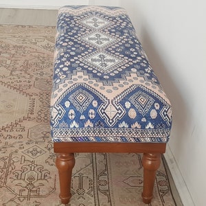 May include: A wooden bench with turned legs and a blue and pink patterned cushion. The cushion has a geometric design with white accents.
