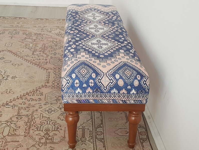 May include: A wooden bench with turned legs and a blue and pink patterned cushion. The cushion has a geometric design with white accents.