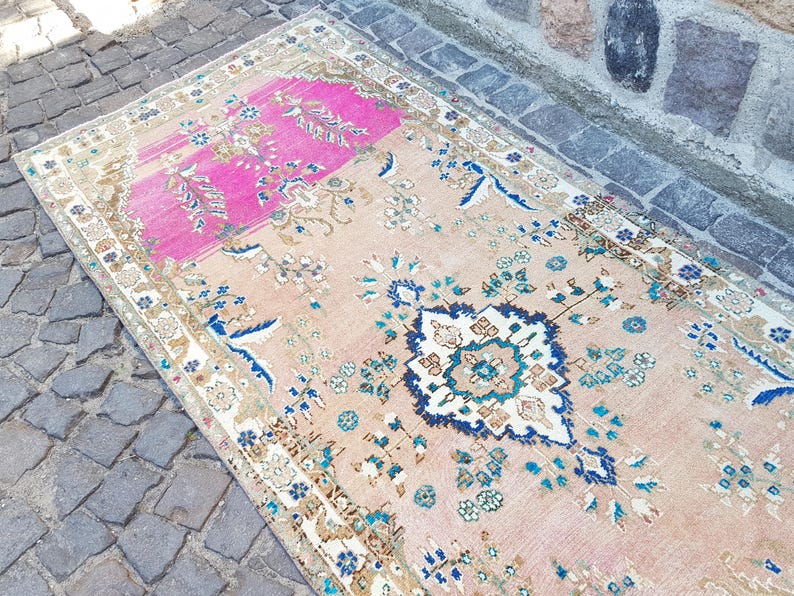 May include: A rectangular area rug featuring a large central medallion in dark blue, light blue, and white, surrounded by floral motifs. The background is a soft peach color with a prominent rectangular section of vibrant hot pink at one end.