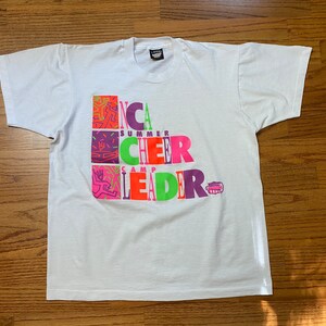 May include: White t-shirt with the text "YMCA SUMMER CHEER CAMP LEADER" in colorful block letters. The design includes geometric figures in pink, orange, green, and purple.