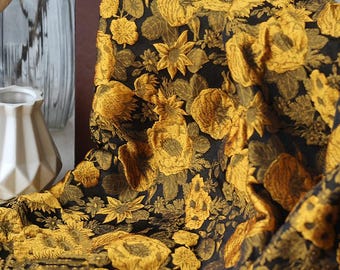 May include: Black fabric with a repeating pattern of yellow flowers and foliage. The floral design features various shapes, including sunflowers and pineapple-like forms. The fabric is draped, showcasing the detailed embroidery and texture.