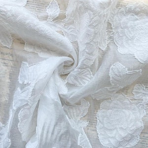 May include: White sheer fabric with an embossed floral pattern. The fabric is delicate and has a soft, flowing texture.