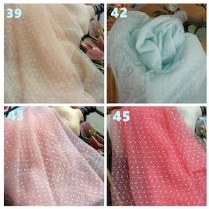 以下が含まれることがあります： 白い水玉模様の透き通った生地のサンプルが4つ。生地はベージュ、水色、ピンク、コーラルの4色で表示されています。