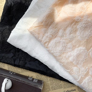 May include: Three pieces of fabric with an embossed floral pattern. The fabric is in black, white, and peach.