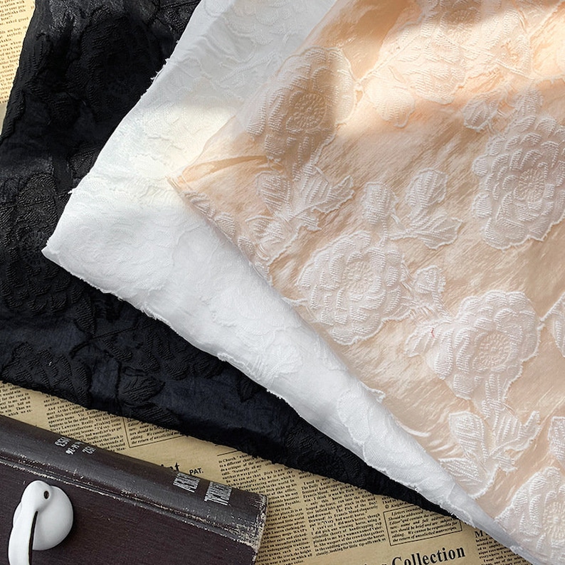 May include: Three pieces of fabric with an embossed floral pattern. The fabric is in black, white, and peach.