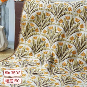 Puede incluir: Tela color crema con un patrón repetido de flores amarillas estilizadas y hojas verdes en un diseño en forma de abanico. La tela tiene el texto "NO: 3502" y "幅宽150" en un recuadro rojo.
