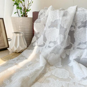 May include: White sheer fabric with an embossed floral pattern. The fabric is draped over a table and has a delicate, romantic look.