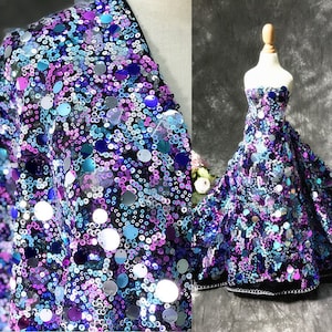 Puede incluir: Un primer plano de una tela con lentejuelas en tonos azules, morados y plateados. Las lentejuelas están dispuestas en un patrón aleatorio y crean un efecto brillante. La tela es perfecta para manualidades, costura y decoración.