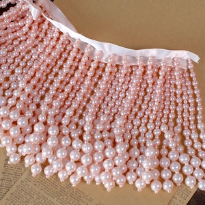 Puede incluir: Borde de perlas rosas con respaldo de satén blanco. El borde está hecho de pequeñas perlas redondas que están enhebradas en filas. El borde es perfecto para agregar un toque de elegancia a cualquier proyecto.