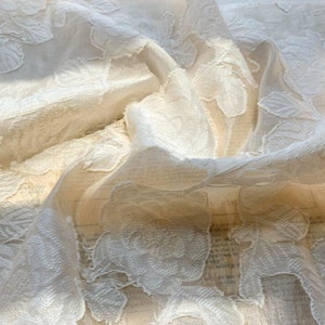 May include: White sheer fabric with an embossed floral pattern. The fabric is delicate and has a soft, flowing texture.