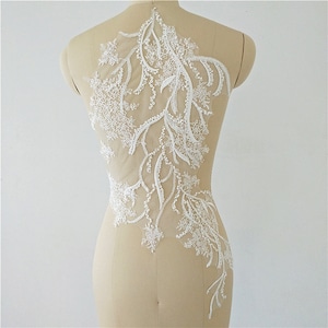 May include: White floral lace applique with a delicate, openwork design. The applique features a flowing, asymmetrical pattern of leaves and flowers, ideal for bridal or craft projects. The lace is displayed on a mannequin.