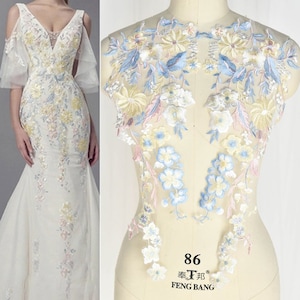 May include: Two pieces of delicate floral lace fabric in shades of blue, yellow, and pink. The lace is on a white background and has a delicate floral pattern. The lace is perfect for adding a touch of elegance to any project.