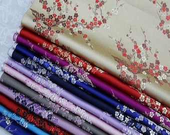 Pode incluir: Uma pilha de rolos de tecido coloridos. O tecido superior é bege com um padrão floral em vermelho, marrom e branco. Abaixo estão rolos em vermelho, roxo, azul e cinza, com desenhos florais e estampados. Os tecidos parecem ser seda ou um material semelhante.
