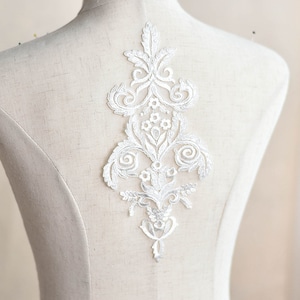 May include: White lace applique featuring a floral design. The applique is ideal for adding a touch of elegance to any garment.