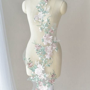 May include: A delicate floral applique featuring pink and white flowers and green leaves on a sheer fabric. The applique is ideal for adding a touch of elegance to clothing, accessories, or home decor.