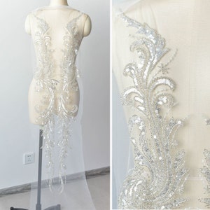 May include: A delicate, beaded lace applique with a floral design. The applique is made of sequins and beads in a silver color and is perfect for adding a touch of elegance to a wedding dress or other special occasion garment.