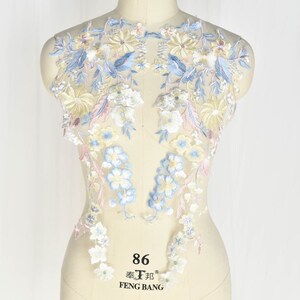 May include: A delicate floral lace applique featuring blue, yellow and pink flowers on a white mesh background. The lace is ideal for adding a touch of elegance to any project.
