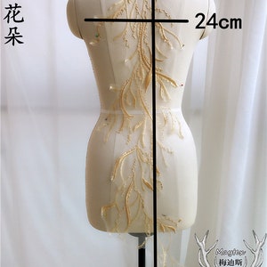 Könnte beinhalten: Goldene florale Spitzenapplikation mit einer Länge von 96 cm und einer Breite von 24 cm. Die Spitze befindet sich auf einem weißen Mannequin.