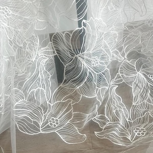 以下が含まれることがあります： 刺繍された花の模様が施された白い透き通った生地。生地は繊細で、柔らかく流れるような質感です。