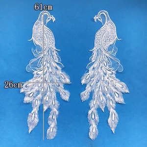 May include: Two white lace peacock appliques, each measuring 61 cm in length and 26 cm in width. The appliques feature intricate details of the peacock's feathers and body.