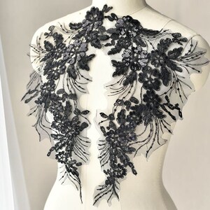 May include: Two black floral lace appliques with sequins and intricate detailing. The appliques are displayed on a mannequin, showcasing their design and texture. The lace features a delicate, open weave.