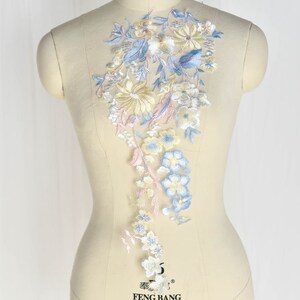 May include: A delicate floral applique featuring blue, yellow and pink flowers and leaves. The applique is ideal for adding a touch of elegance to clothing, accessories or home decor.