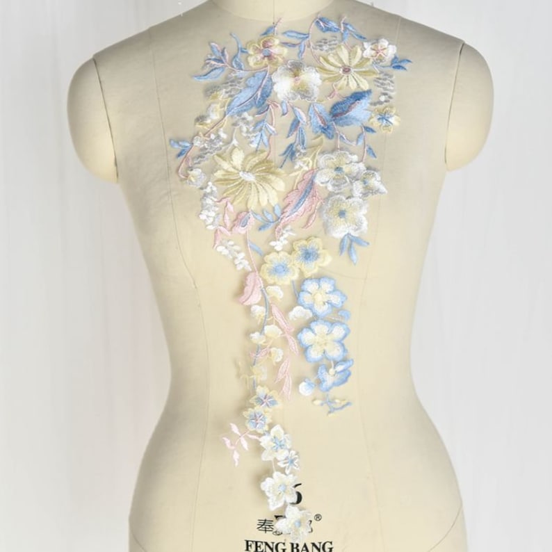 May include: A delicate floral applique featuring blue, yellow and pink flowers and leaves. The applique is ideal for adding a touch of elegance to clothing, accessories or home decor.