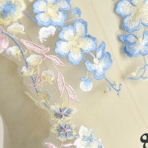 May include: Delicate floral embroidery featuring light blue, yellow, and pink flowers on a sheer white fabric. The embroidery is ideal for adding a touch of elegance to any project.