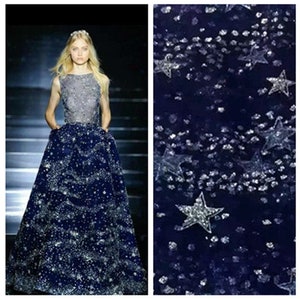 Puede incluir: Una tela de tul azul marino con purpurina plateada y lentejuelas en forma de estrella. La tela es perfecta para crear un look glamuroso y festivo.