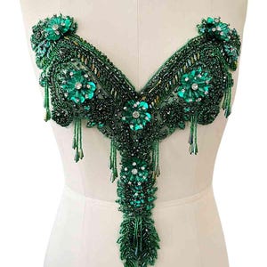 Op de afbeelding: Een groene kralenversiering met een V-hals en hangende kralen. De versiering is gemaakt van groene kralen en strass.