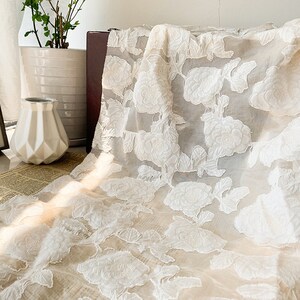 May include: White sheer fabric with an embroidered floral pattern. The fabric is delicate and has a soft, flowing texture.