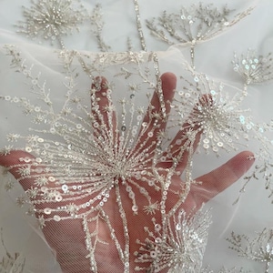 May include: White tulle fabric with silver sequins and beads embroidered in a dandelion design.