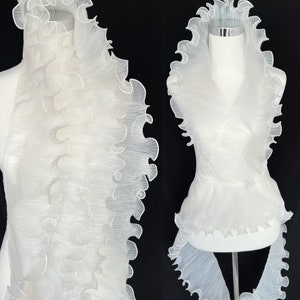 May include: White ruffled fabric top with a high neckline and a fitted bodice. The top has a unique design with multiple layers of ruffles.