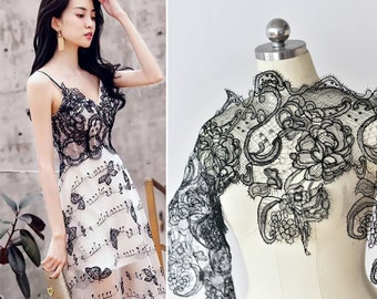 May include: Black lace fabric with a floral design. The lace is delicate and intricate, with a scalloped edge. It is perfect for adding a touch of elegance to any project.