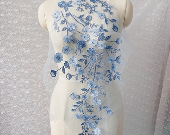 Può includere: Applique di ricamo floreale blu su un tessuto bianco trasparente. Il design presenta delicati fiori e foglie in un motivo a cascata.