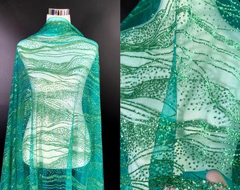 May include: Green sparkly fabric with a wavy pattern. The fabric is sheer and has a delicate texture.