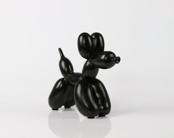 May include: A glossy black sculpture shaped like a balloon animal dog. The figure features rounded, inflated-looking segments forming the head, ears, body, four legs, and a pointed tail, all finished with a smooth, reflective surface texture.