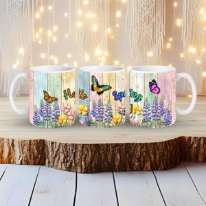 Peut inclure: Trois mugs en céramique blanche avec un motif printanier. Chaque mug présente un motif floral et papillon coloré avec les mots "Hello Spring" imprimés. Le fond a un motif de planches de bois aux couleurs pastel.