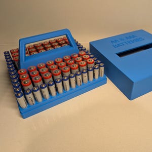 May include: A blue battery storage case filled with AA and AAA batteries. The batteries are red, white, and blue. A matching blue lid with the text "AA & AAA BATTERIES" is next to the organizer.
