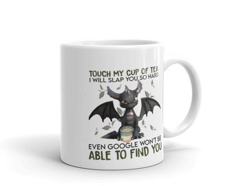 Puede incluir: Taza de cerámica blanca con un diseño de dragón de dibujos animados y el texto "TOUCH MY CUP OF TEA I WILL SLAP YOU SO HARD EVEN GOOGLE WON'T BE ABLE TO FIND YOU". El dragón es negro con alas.