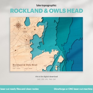 Op de afbeelding: Een houten topografische kaart van Rockland & Owls Head, Maine, VS. De kaart toont lasergesneden details van de kustlijn en omgeving, met blauwe en turquoise waterelementen. Tekst omvat "lake topographic" en "ROCKLAND & OWLS HEAD".