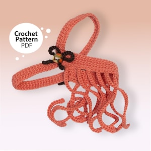 以下が含まれることがあります： 「Crochet Pattern PDF」の文字が入った、コーラル色の編み物パターン。編み物のデザインは、ハンドル、ぶら下がっているループのある装飾部分、金色のアクセントが付いた茶色のリボンが特徴です。