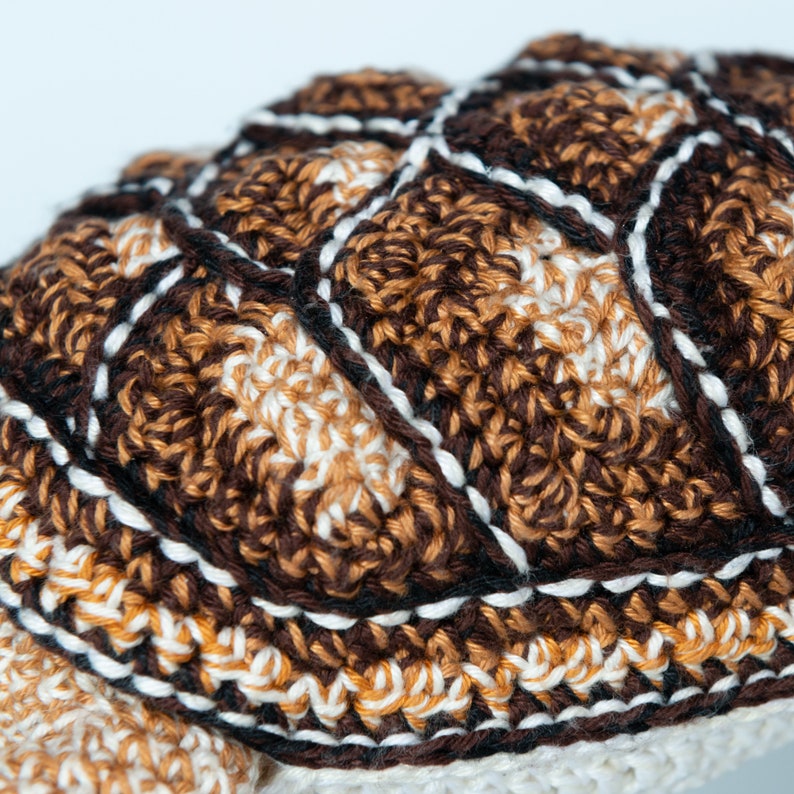 May include: Close-up of a crocheted brown, white, and black patterned fabric. The fabric has a textured, woven appearance.